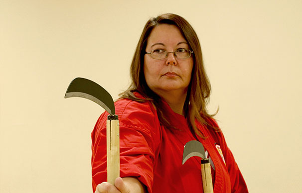 a woman is focused and concentrated. she has two curved bladed weapons called kamas in her hands. She has glasses and long hair