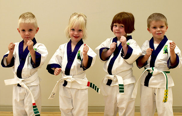 Four small children aged three to four stand together with their fists raised. They are all smiling and happy.